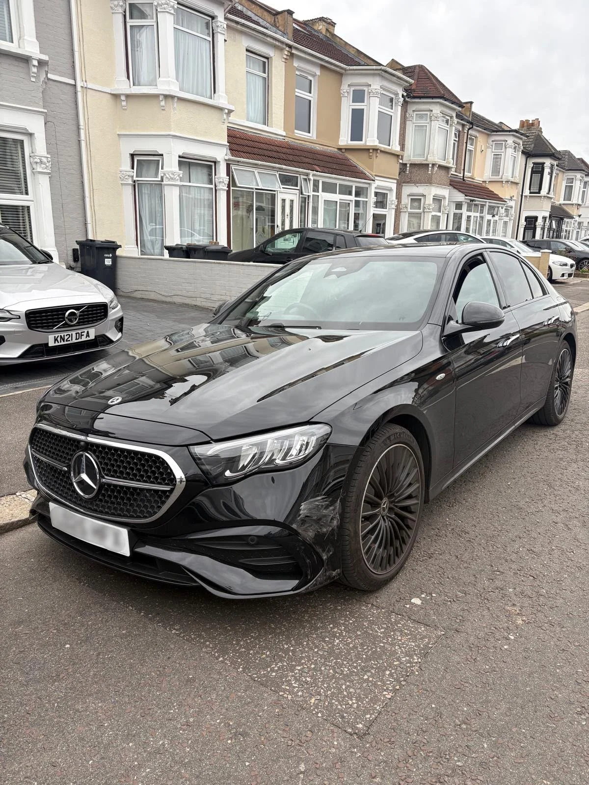 Black Mercedes E-Class with deep scuffs and scraped paint along the front bumper corner before repair