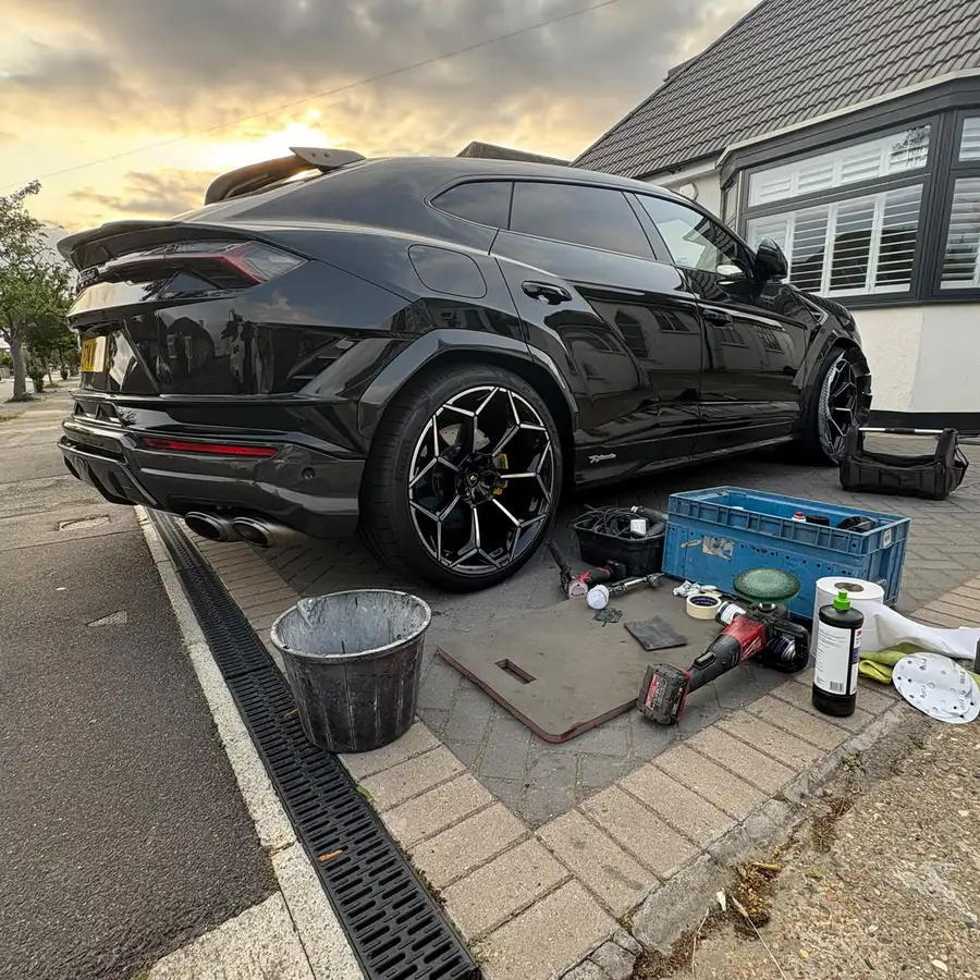 Lamborghini Urus on a driveway at sunset during a mobile alloy wheel repair, with tools and polishing kit laid out alongside